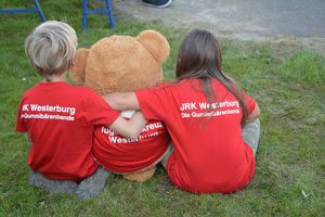 Zwei Kinder umarmen sitzen einen großen Teddybären.